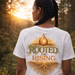 Person wearing a white t-shirt with 'Rooted and Rising' design in a natural setting.